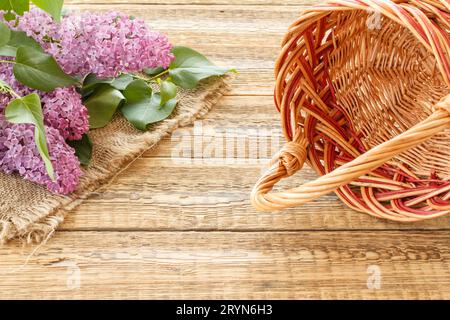 Lilac flowers with a wicker basket on the wooden boards. Stock Photo