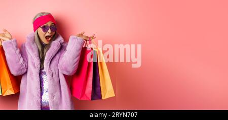 Stylish asian senior woman going shopping, wearing trendy clothes and sunglasses, holding store bags with gifts, treat yourself Stock Photo