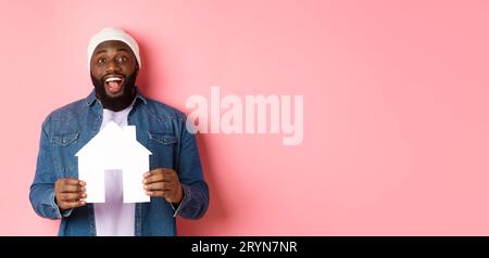 Real estate concept. Happy smiling african-american man holding house model, looking excited at camera, searching for home, stan Stock Photo