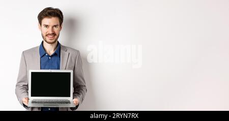 Handsome caucasian businessman in suit showing empty laptop screen, demonstrate promo, standing on white background Stock Photo