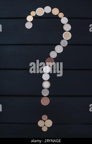 Scattered coins of different countries in the form of a question mark point on wooden table. finance concept Stock Photo