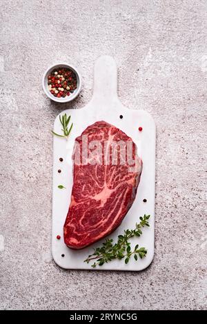 Fresh marbled beef rib eye steak and spices on grey stone background Stock Photo