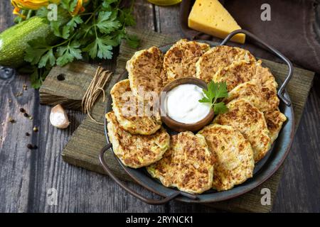 Healthy summer food, zucchini fritters. Vegetarian zucchini pancakes with cheese, served with sour cream on a rustic wooden tabl Stock Photo
