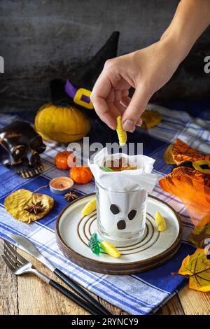 Halloween party. White ghost crafts scary face in glass on a plate and a festive Halloween table setting with pumpkins. Stock Photo
