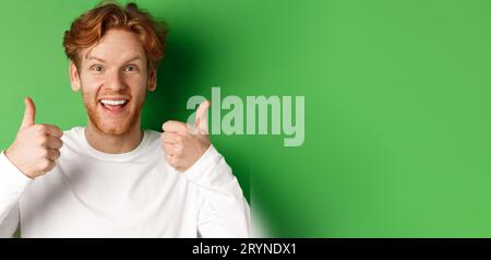 Emotions and fashion concept. Close up of cheerful redhead man showing thumbs-up and say yes, approve and like something cool, g Stock Photo
