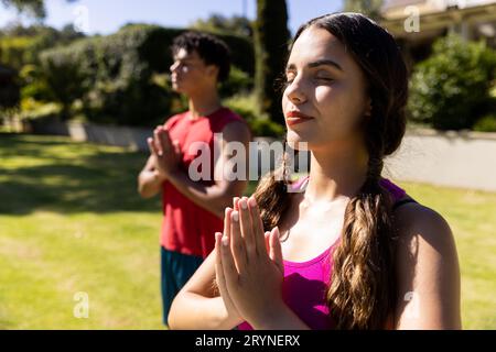 Biracial young girlfriend with boyfriend meditating in prayer pose while standing in yard Stock Photo