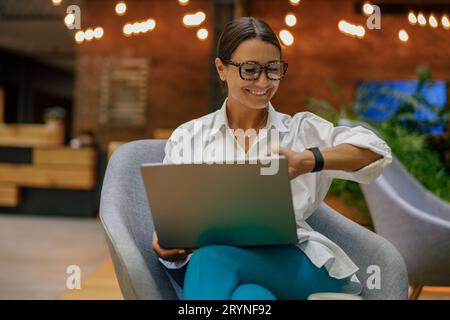 Female manager looking time on wrist watch while working laptop on modern office background Stock Photo