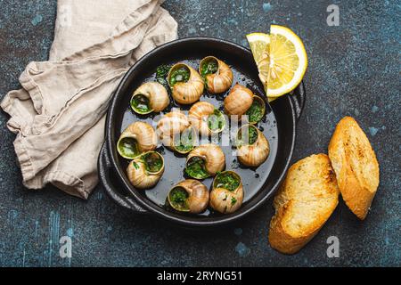 Escargots de Bourgogne Snails with Garlic Butter and Parsley in black cast iron pan with Lemon and Toasted Baguette Slices on ru Stock Photo