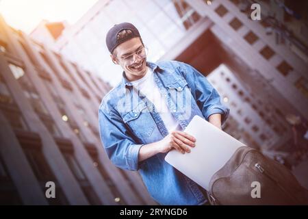 Smart attitude. Positive handsome man using a laptop and sitting in the street while surfing the internet have a web conference. Stock Photo
