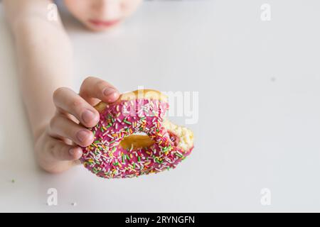 Children's hand stretches a bitten donut in a pink glaze Stock Photo