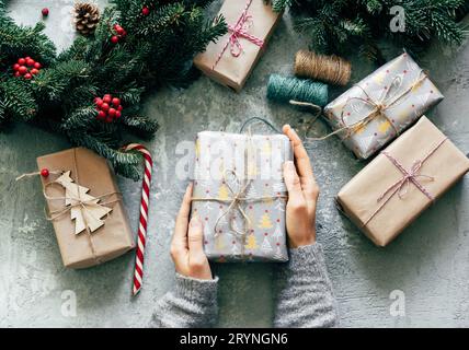 Top view of hands holding Christmas gift boxes. New Year's decor on the table. Christmas fir wreath Stock Photo