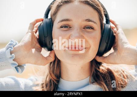 Face of pretty young woman listening to music with wireless headphones outside in nature. Woman with wireless headset on her ear Stock Photo