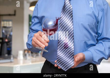 A man holding a wine glass in his hand and is letting some of vine drip onto his tie. Stock Photo