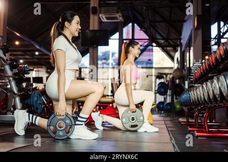 Two young asian woman doing exercises with heavy weights plates in gym. Stock Photo