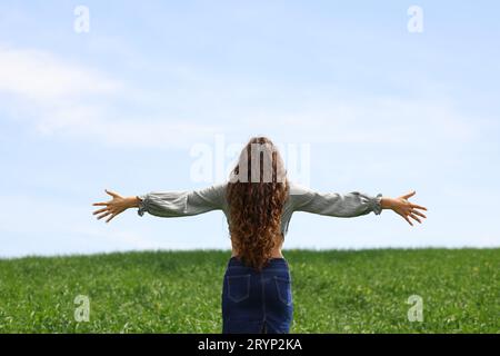Back view of a happy woman celebrating vacation outstretching atms in a field Stock Photo