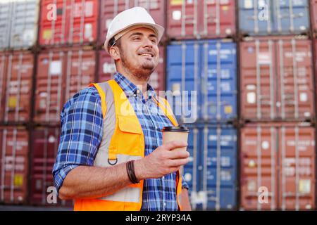 Young man engineer with coffee in container warehouse. Logistics management in container yard. Stock Photo