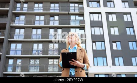 Woman entrepreneur looks around making notes on clipboard Stock Photo