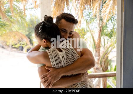 Loving caucasian young couple embracing while standing in balcony seen through cottage doorway Stock Photo