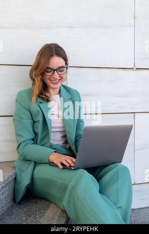 Business woman sitting on stairs outside office building while working with laptop Stock Photo