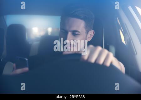 Photo of a handsome man using mobile phone while driving. Stock Photo