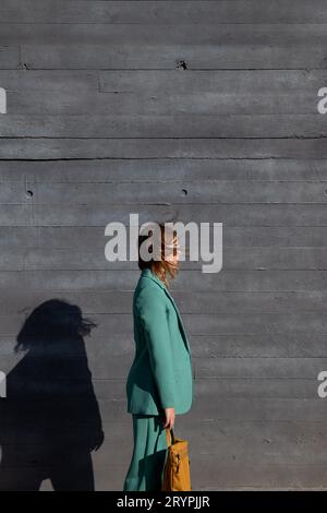 Stylish business ginger-haired woman in green suit, white sunglasses and yellow backpack standing on black background Stock Photo