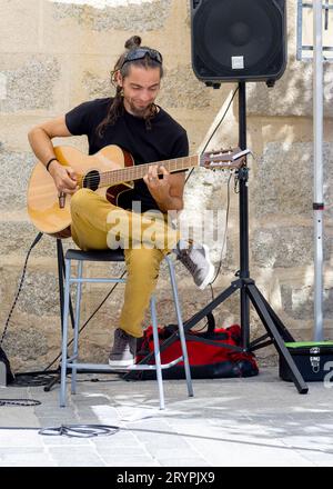 man sitting on a stool in an outdoor setting, playing an acoustic guitar Stock Photo