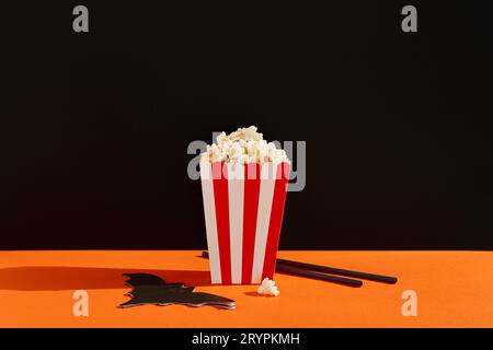 Striped box with popcorn, bat napkin and straws on an orange black background Stock Photo