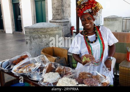 Bahian woman in traditional white dress (Baiana) selling street food at the Pelourinho district, Salvador, Bahia, Brazil. Stock Photo