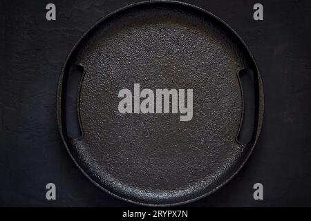Empty rustic cast iron plate On a black background. Top view wit Stock Photo
