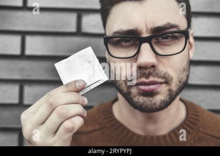Portrait of a smiling casual man holding condom over brick wall Stock Photo