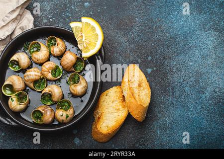 Escargots de Bourgogne Snails with Garlic Butter and Parsley in black cast iron pan with Lemon and Toasted Baguette Slices on ru Stock Photo