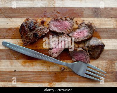 Ready to eat a beef steak cut in to slices with a fork on a wooden cutting board. Stock Photo