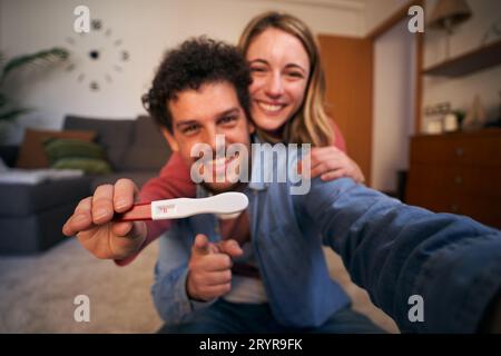 Selfie mobile smiling young Caucasian couple looking joyful at camera holding positive pregnancy. Stock Photo