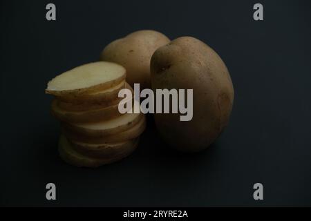 stacked and whole potato slices on black background. Stock Photo
