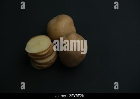 stacked  potato slices and whole potatos on black background. Stock Photo