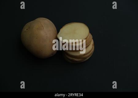 whole potato and stacked  potato slices on black background. Stock Photo