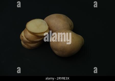 stacked  potato slices and whole  potatos on black background. Stock Photo