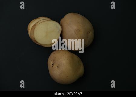 Whole potato and stacked  potato slices on black background. Stock Photo