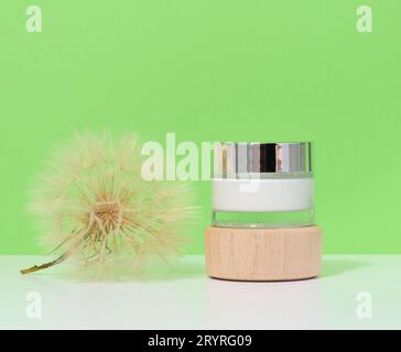 Glass jar with cream and dandelion on a green background, skin care cosmetics Stock Photo