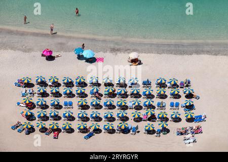 Holiday makers relaxing on a sunny beach in Amadores, Gran Canaria, Spain. Sun loungers are arranged neatly under colourful parasols close to the sea Stock Photo