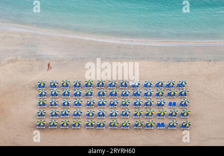 Sun loungers are arranged neatly in rows under colourful parasols close to the sea on a sunny beach in Amadores, Gran Canaria, Spain. Stock Photo