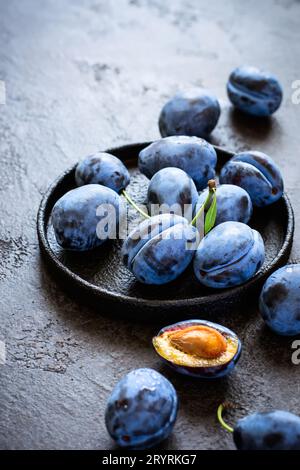 Dark blue plums in cast iron plate on black background closeup Stock Photo