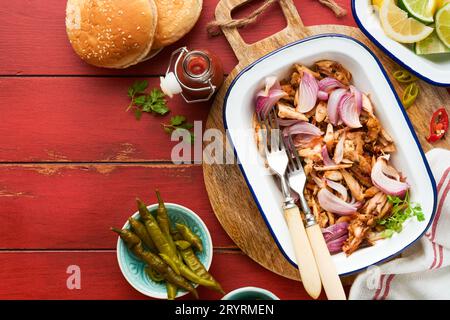 Pulled bbq chicken with baked onions on serving platter, bbq corn, pickles, chili peppers and buns for hot dogs and burgers, tomato sauce. Traditional Stock Photo
