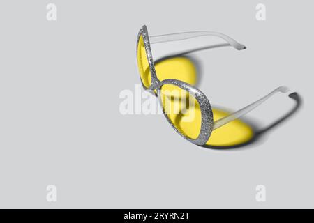 Trending colors of 2021. Plastic sunglasses with silver sparkles frame and yellow glasses. Yellow color shadow from glasses Stock Photo