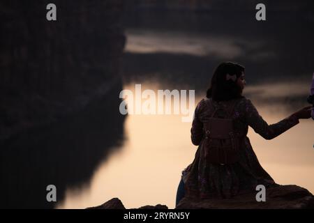 A view from the back of a tourist girl sits on a mountain and admires the beautiful view and dawn or sunset or sunrise. Woman sitting on a rock over m Stock Photo