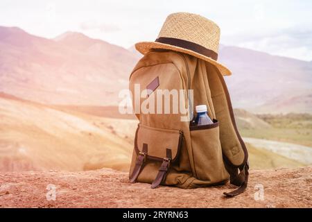 Beige backpack, bottle of water and straw hat on on top of the mountain. Active travel concept. Toning sunrise Stock Photo