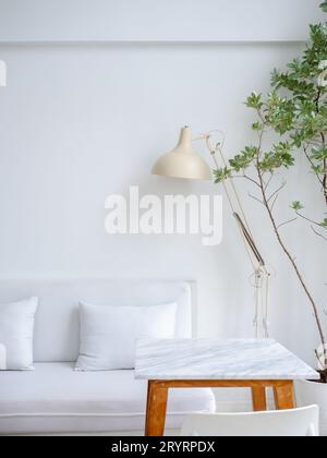 Modern relaxing and clean living room corner decoration with white couch or sofa seat with pillows, beige table light lamp near empty marble top table Stock Photo
