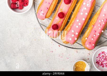Delicious eclairs with pink glaze, raspberry and sugar sprinkles on gray background Stock Photo