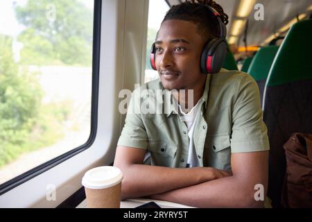 Young Man Commuting To Work Sitting  On Train Wearing Wireless Headphones Stock Photo