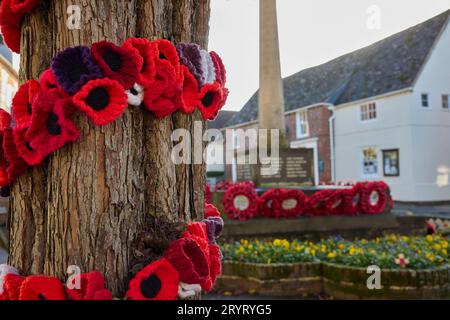 Knitted Poppies Around Tree For Remembrance Day With War Memorial And Poppy Wreaths In Background Stock Photo